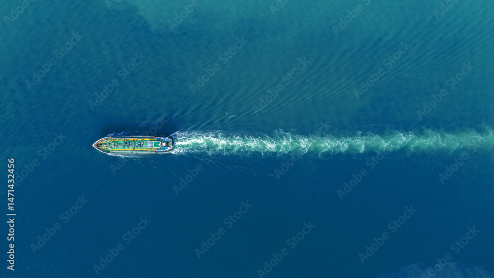 Obraz premium Aerial view of an oil tanker ship sailing through calm blue ocean water, leaving a visible white wake behind. Concept of global transportation, marine logistics, and energy shipping.