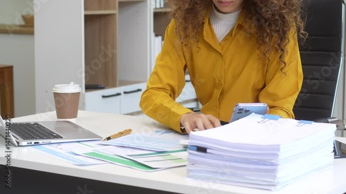 Confident Russian businesswoman sits indoors at her desk, dressed in formal attire,  paperwork and planning. Stylish and efficient, she manages tasks, notes ideas, and leads with professionalism.