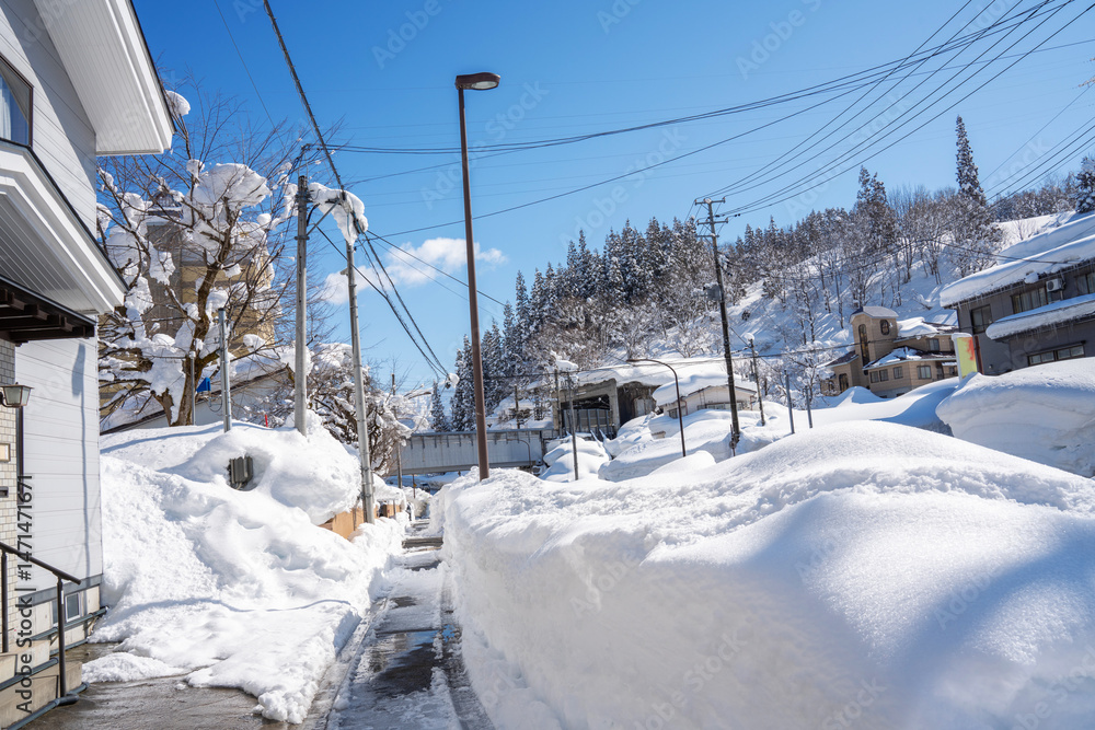 A peaceful winter village nestled in a snow-covered mountain landscape. Thick layers of snow blanket rooftops, streets, and trees under a bright blue sky, capturing the quiet charm of a serene A peaceful winter village nestled in a snow-covered mountain landscape. Thick layers of snow blanket rooftops, streets, and trees under a bright blue sky, capturing the quiet charm of a serene