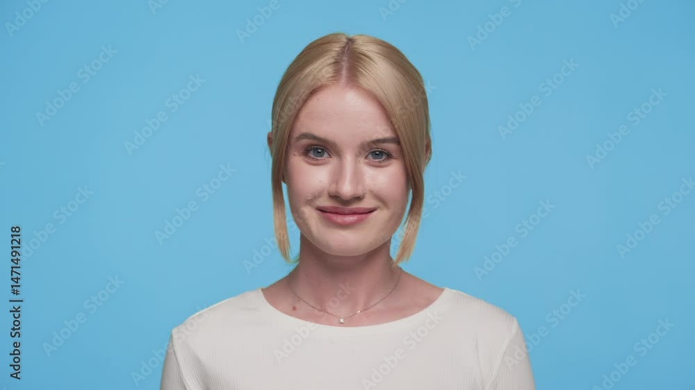 Confident young woman winking playfully at camera on blue