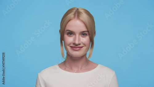 Confident young woman winking playfully at camera on blue