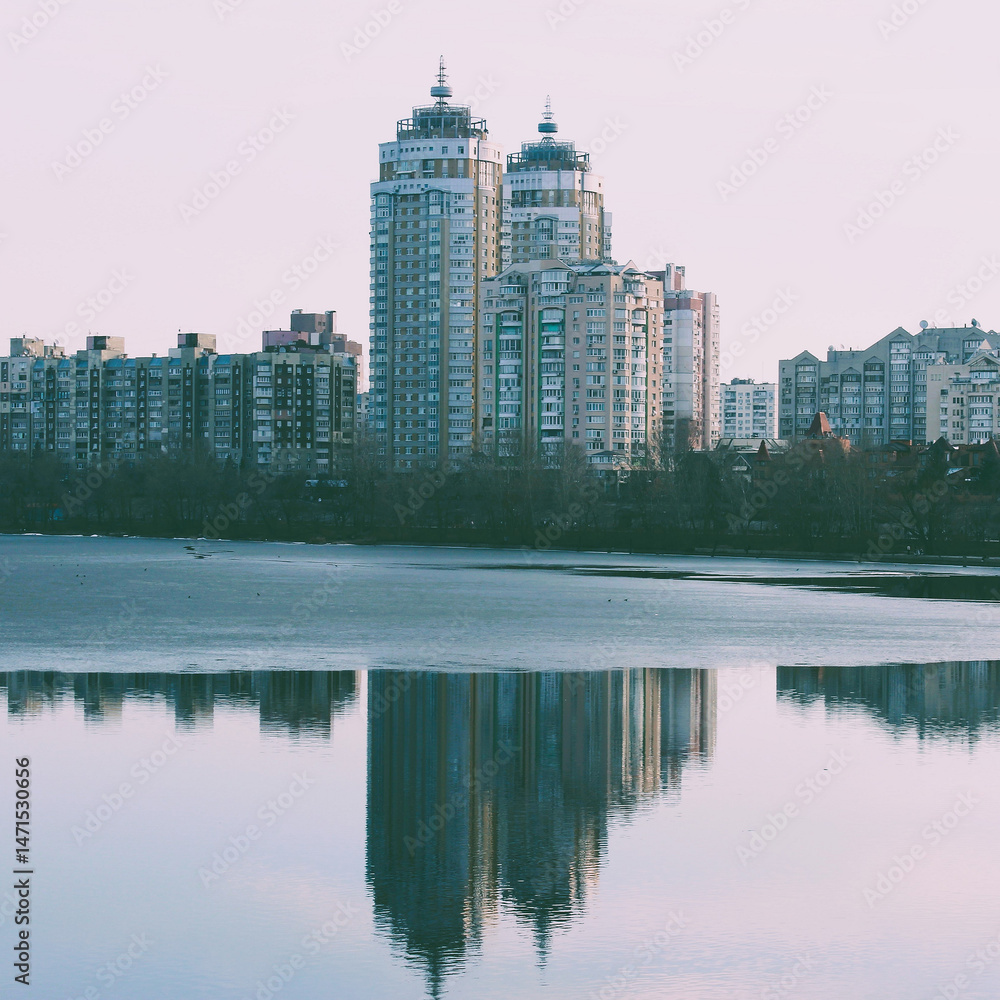 Fototapeta premium Square Stock Photo of City Buildings Near River Shore Reflects in Calm Water