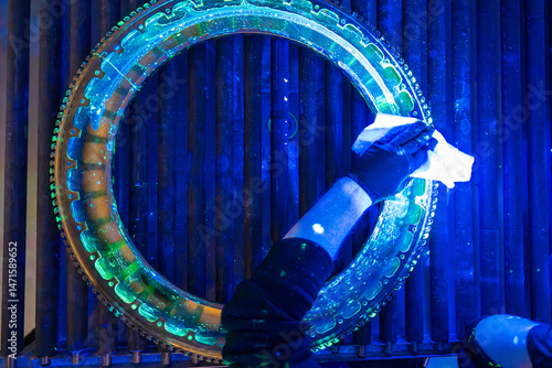 Part undergoing fluorescent penetrant inspection with technicians gloved hand wiping test surface. Advanced NDT process illuminates potential flaws in aerospace component with a distinctive green glow