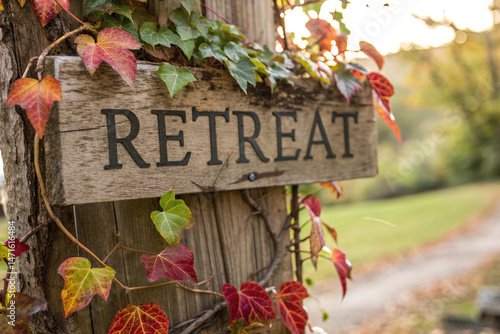Rustic wooden sign indicating a retreat with colorful leaves and blurred background.