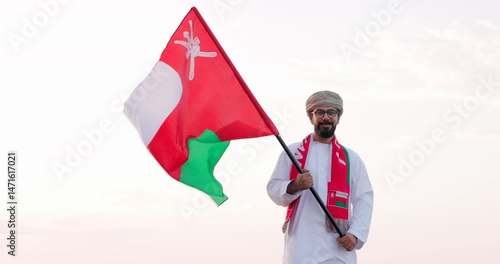 Omani man stands with Omani National Flag, wearing omani traditional dishdasha and Musaar