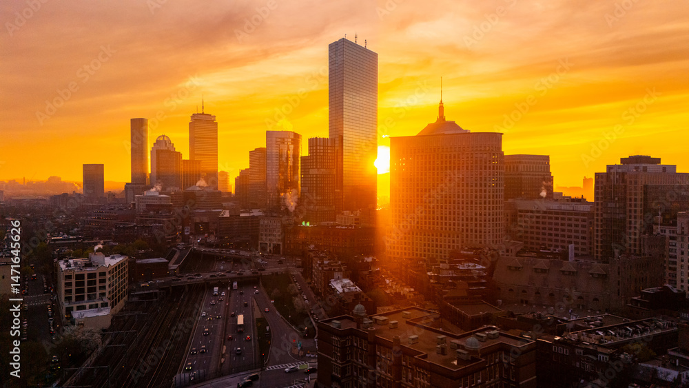Obraz premium Golden hour in the lively modern city. Setting sun hides behind the towers of Boston, Massachusetts, USA. Orange sky at backdrop. Aerial view.