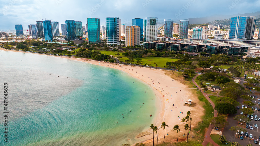Naklejka premium Beautiful sandy beach surrounded by green park. Modern high-rise buildings of Waikiki at backdrop. Hawaii, USA.