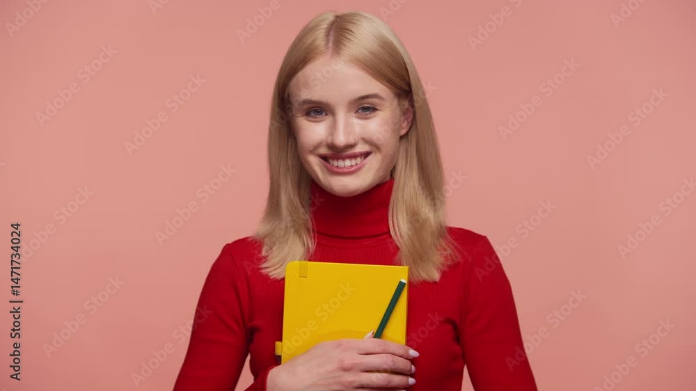Smiling student holding notebook and pencil on pink background Smiling student holding notebook and pencil on pink background
