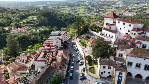 Aerial 4K footage of the National Palace of Sintra, Portugal. Smooth drone flight over historic white building with iconic chimneys, green hills, and traditional architecture