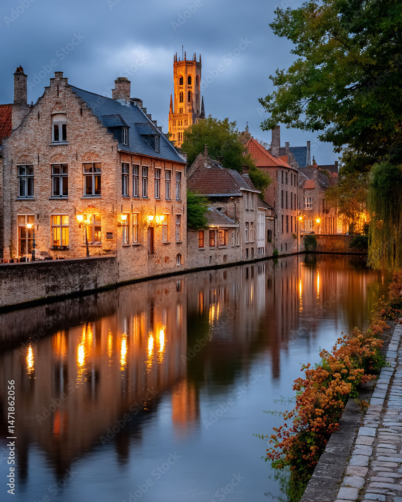 Fototapeta premium Stone buildings glow along a canal reflecting lights in a vintage town at dusk