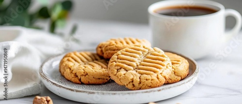 Plate of freshly baked peanut butter cookies on a white marble table. the cookies are golden brown and have a criss-cross pattern on top. they are arranged in a circular pattern on the plate.