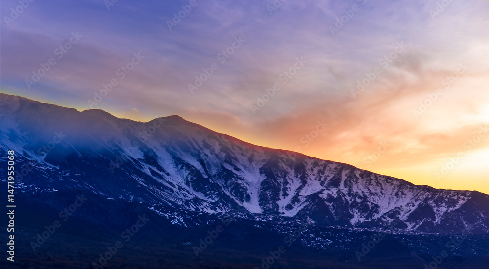 Obraz premium highland mountain landscape of beautiful sunset or sunrise behind nice mountain peaks and slopes in snow and majestic cloudy sky on background