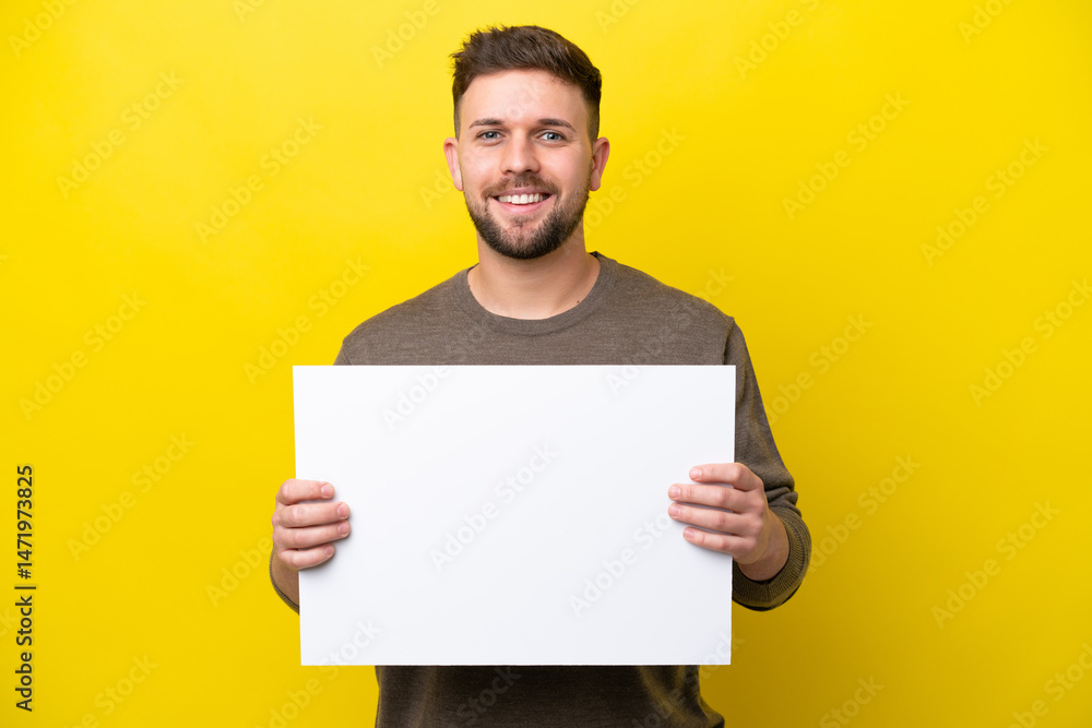 Young caucasian man isolated on yellow background holding an empty placard with happy expression Young caucasian man isolated on yellow background holding an empty placard with happy expression