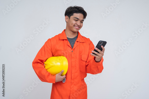 Young Southeast Asian male worker smiling while holding a phone, symbolizing sending remittance money to family through mobile banking. Isolated on a light background.