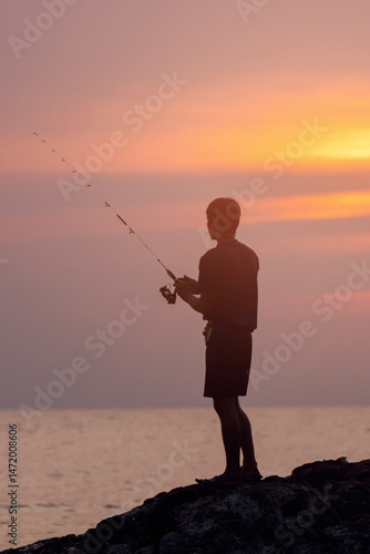 A man fishing from a cliff in the evening, and looking into the distance, admiring the sunset and watching the bite. Rear view close-up vertical photo lifestyle.