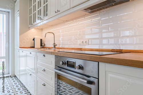Bright kitchen with white cabinets, wood counters, stainless steel oven, and glossy white tile backsplash