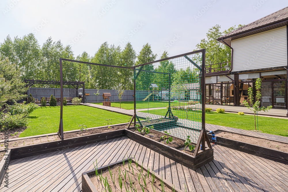 Lush green backyard with raised garden beds, a lawn, and a modern house on a sunny day. Lush green backyard with raised garden beds, a lawn, and a modern house on a sunny day.