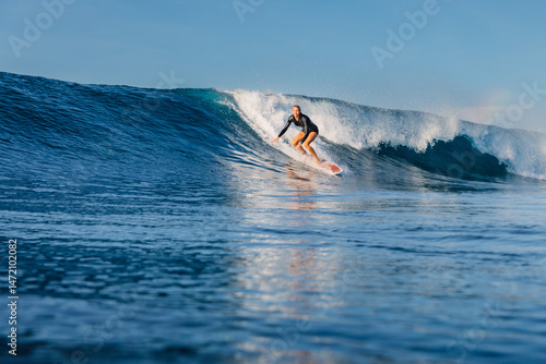 Photography Surfer woman riding on breaking blue wave, surfing in Bali.