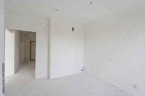 empty  all-white room with a doorway leading to another space. The walls are plain  and the floor is bare. Minimalist and clean aesthetic.