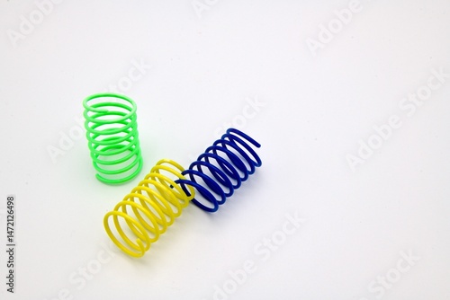 green, yellow and blue plastic spring on white background. cat toys