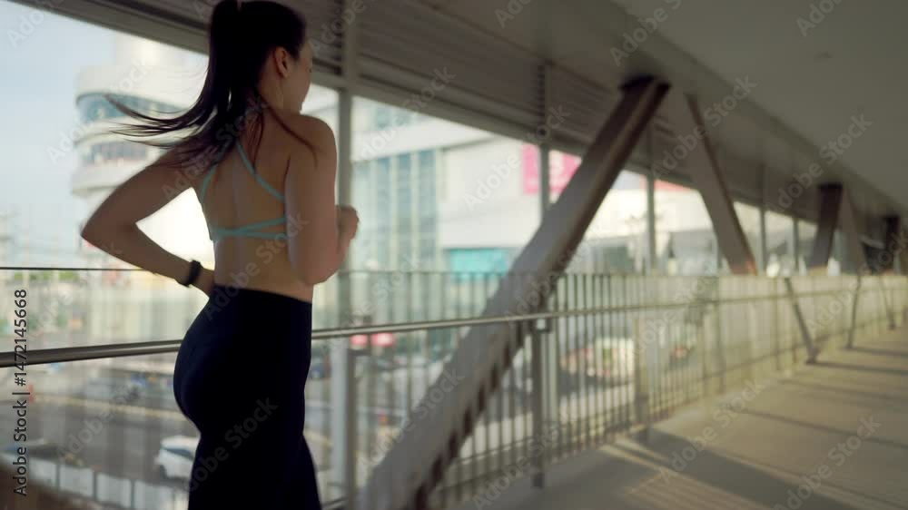 A woman is running in a long hallway. She is wearing a black top and black pants. The hallway is very long and has a lot of windows A woman is running in a long hallway. She is wearing a black top and black pants. The hallway is very long and has a lot of windows