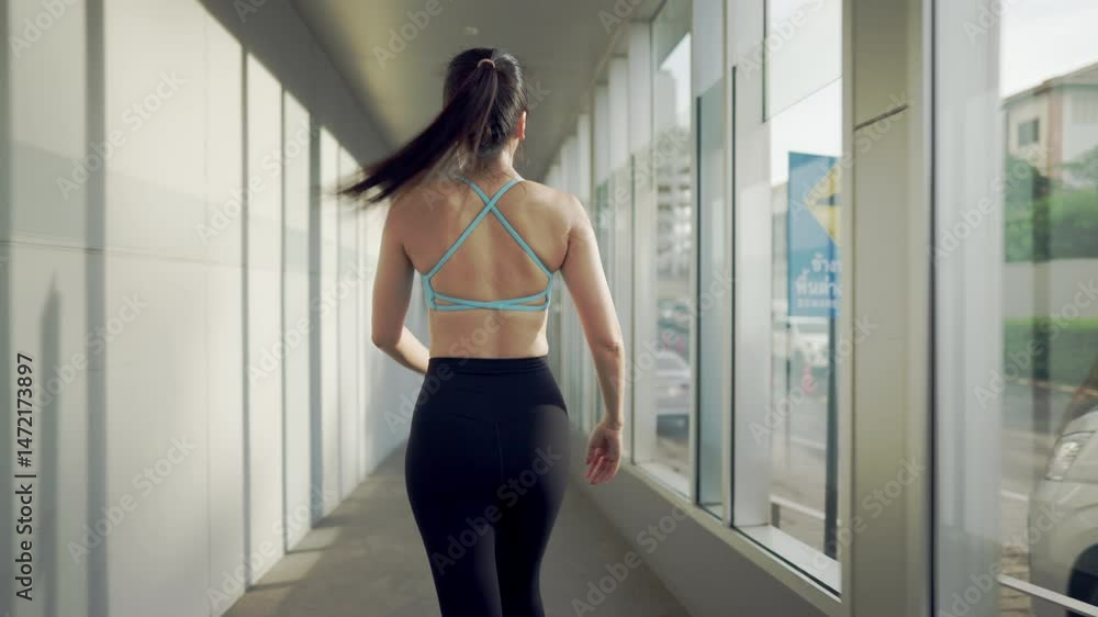 A woman is running in a hallway with a car outside. She is wearing a blue shirt and black pants A woman is running in a hallway with a car outside. She is wearing a blue shirt and black pants