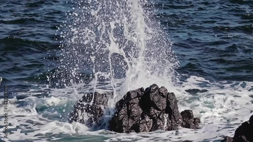 Powerful ocean waves crash against jagged rocks, creating dramatic splashes and showcasing the raw power of nature