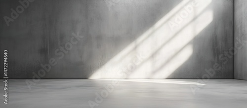 Empty gray cement-walled room with diagonal sunlight shadows.