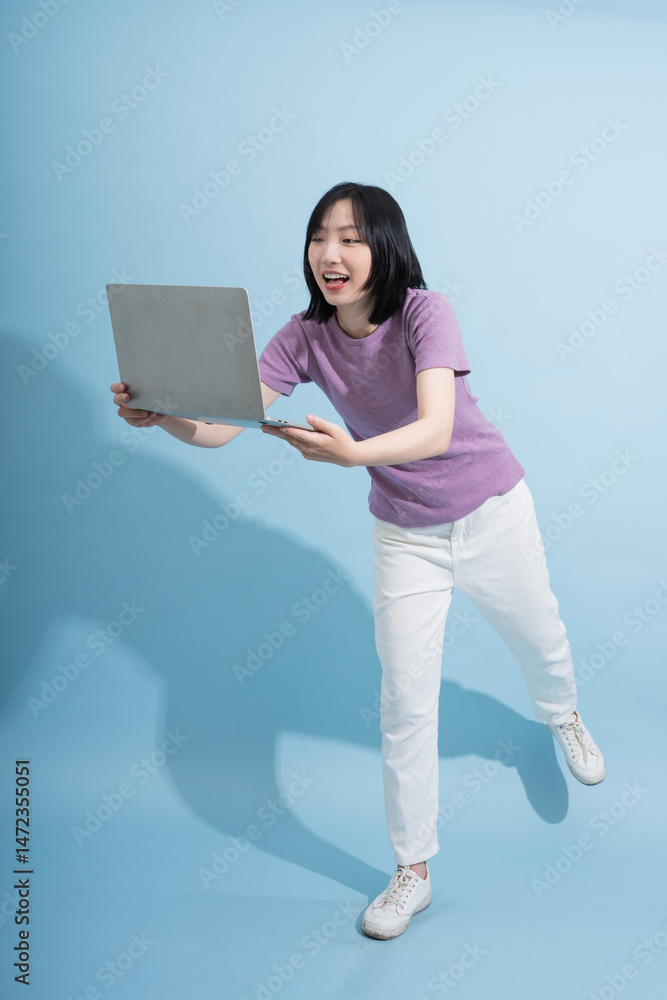 Enthusiastic young woman interacting with laptop on blue background while engaging in a creative activity Enthusiastic young woman interacting with laptop on blue background while engaging in a creative activity