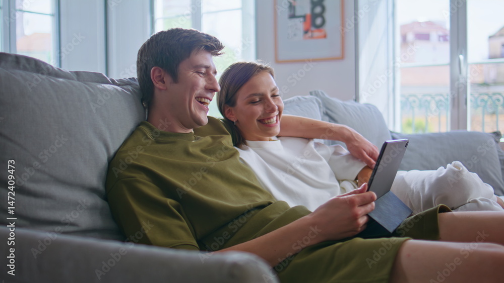 Embracing lovers using tablet laughing at home closeup. Positive couple cuddling