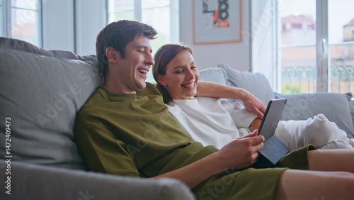 Obraz na płótnie Embracing lovers using tablet laughing at home closeup. Positive couple cuddling w salonie