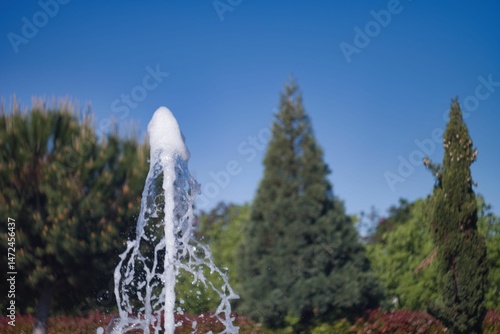 Fountain water splashes under a clear blue sky in a beautiful park during a sunny day
