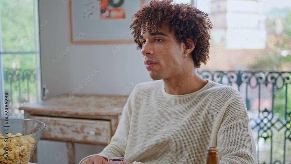 Curly guy eating popcorn enjoying board game closeup. Students chilling together