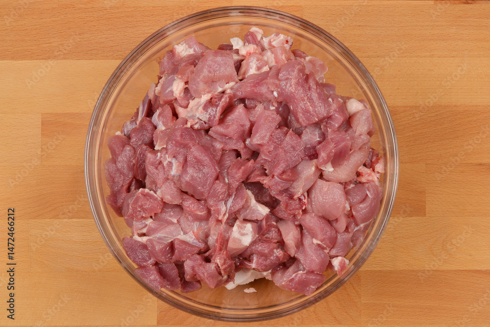 A clear glass bowl filled with diced raw pork sits on a wooden cutting board