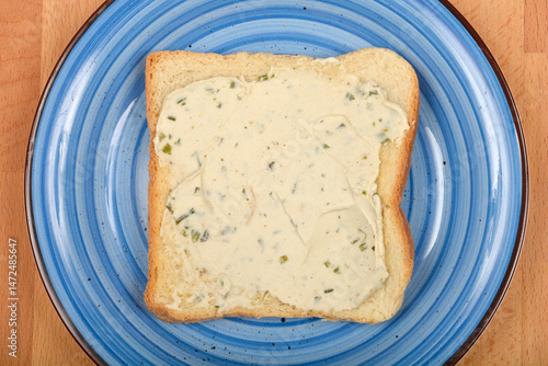 A slice of bread topped with creamy vegan cheese and green herbs rests on a blue swirled plate