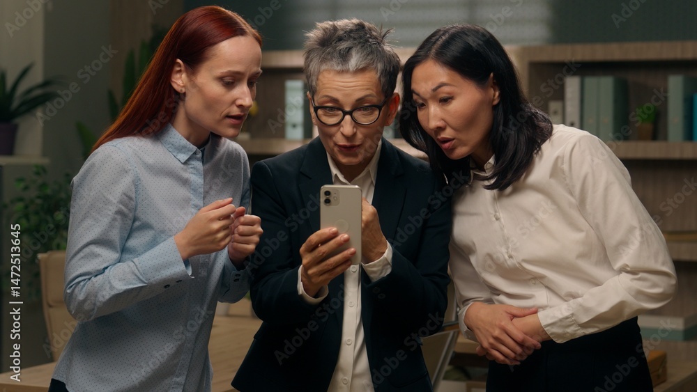 Obraz premium Happy excited women colleagues team group holding mobile phone multinational read good news businesswomen winning online finance celebrating office success offer ladies bet multiracial business people
