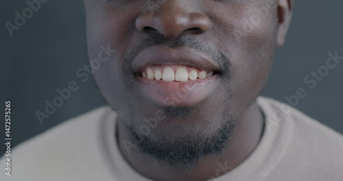 Close-up slow motion portrait of African American man's mouth smiling on black color background. Good mood and happy person concept.