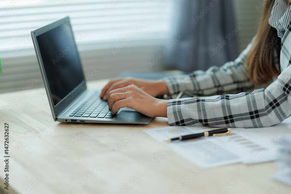 Fototapeta premium Professional female accountant reviewing annual expense reports at her desk with a laptop and paperwork — ideal for finance, tax, and corporate business themes.