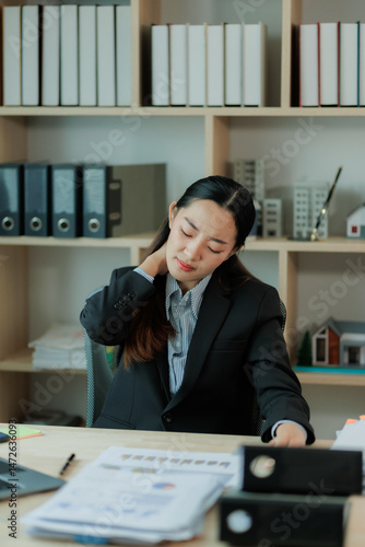 Quadro em tela After hours of focused laptop work, a young Asian businesswoman stretches at her desk to ease tension and support good posture in the office