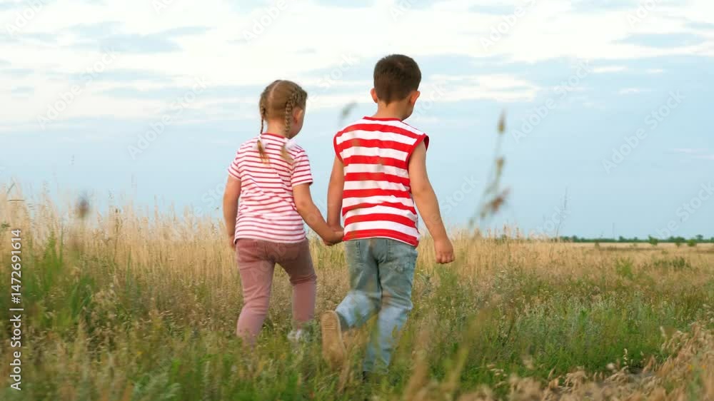 Joyful toddlers boy and girl run holding hands along rural road with wild grass backside view. Boy and girl siblings play actively at summer pastureland. Little boy and girl run and enjoy freedom Joyful toddlers boy and girl run holding hands along rural road with wild grass backside view. Boy and girl siblings play actively at summer pastureland. Little boy and girl run and enjoy freedom