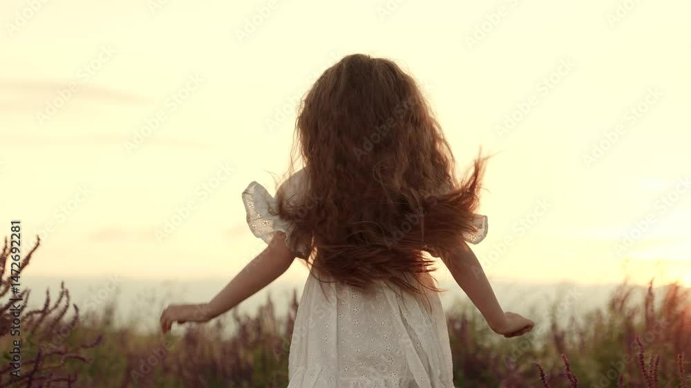 Little girl expresses happiness with dance in wild field at summer sunset backside view. Little girl dances playing in rural field on summer holiday. Joyful little girl dances in field at sunset Little girl expresses happiness with dance in wild field at summer sunset backside view. Little girl dances playing in rural field on summer holiday. Joyful little girl dances in field at sunset