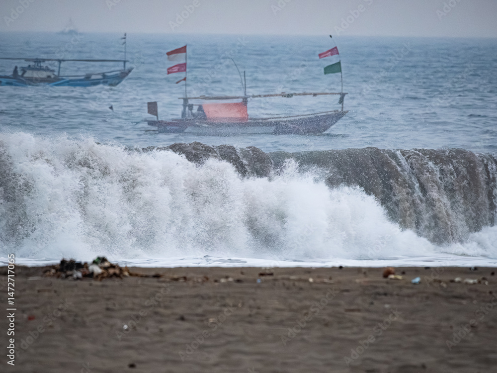 Naklejka premium Fishermen are forced to go to sea to look for fish amidst very large waves on the southern coast of Java due to changes in the earth's climate.