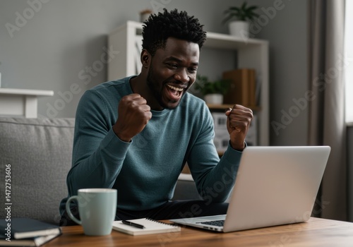 A joyous african american man celebrates a victory while using his laptop at home.
