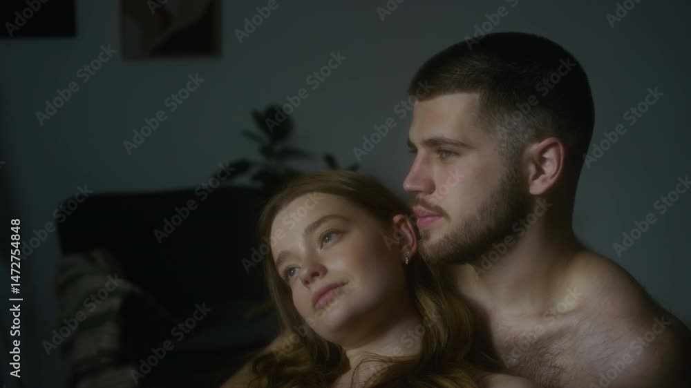 Close-up low key shot of young Caucasian couple hugging and looking out of window after sleep in morning in bedroom, man embracing girlfriend from behind, showing deep affection and love Close-up low key shot of young Caucasian couple hugging and looking out of window after sleep in morning in bedroom, man embracing girlfriend from behind, showing deep affection and love