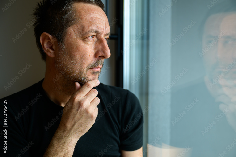 Fototapeta premium Serious caucasian mature adult male looking through window and thinking
