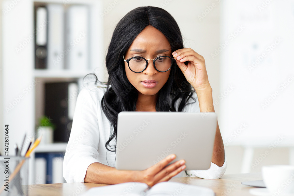 Serious female entrepreneur working on tablet computer at office, participating in webinar or online conference at office. Worried black business lady solving work problem through internet Serious female entrepreneur working on tablet computer at office, participating in webinar or online conference at office. Worried black business lady solving work problem through internet