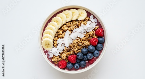 Açai Bowl Topped with Banana, Granola, Coconut Flakes and Berries in White Bowl on White Background in High-Resolution Top-Down Photograph Emphasizing Vibrant Colors