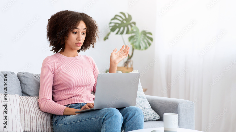 Stressed attractive lady annoyed by hard job, task or system crash, problems at work. Frustrated shocked young african american female sits on sofa with cup, holds laptop and gestures with hand Stressed attractive lady annoyed by hard job, task or system crash, problems at work. Frustrated shocked young african american female sits on sofa with cup, holds laptop and gestures with hand