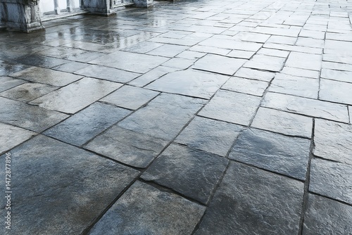 Wet stone pavement with reflections and blurred background architectural elements.