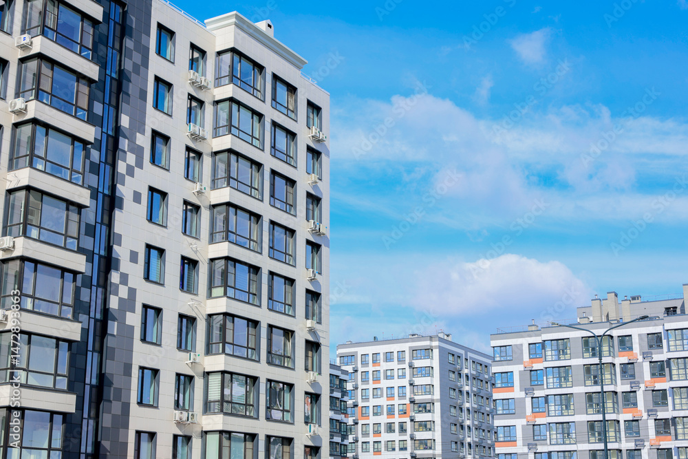 Fototapeta premium Multi-storey residential buildings of modern architecture with large windows and balconies against the background of the sky and clouds. 